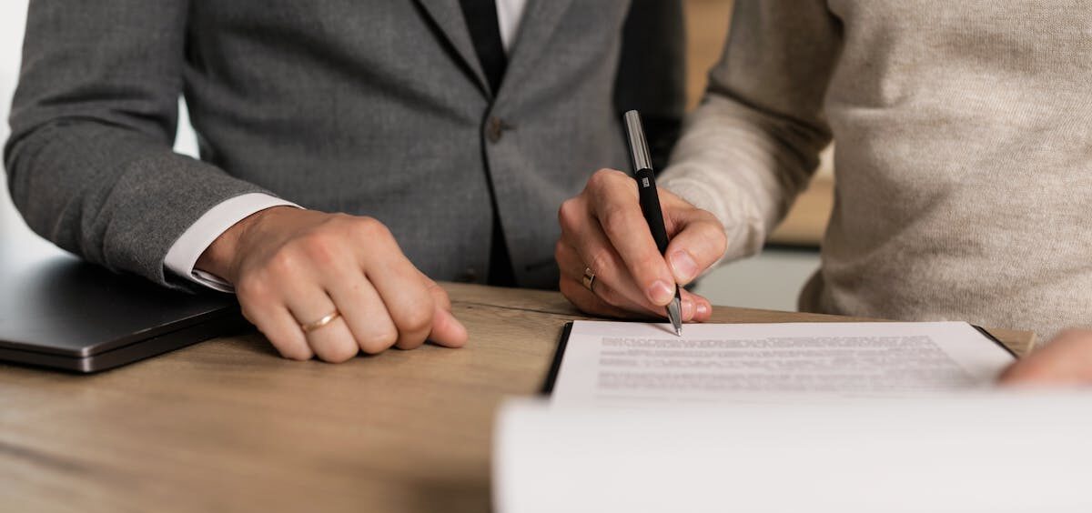 Close-up of businessmen signing documents at a wooden table in an office.